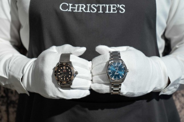 A Christie's employee holds a pair of Omega watches worn by actor Daniel Craig in the film "No Time To Die" during a photocall ahead of the "Sixty Years of James Bond" auction at Christie's auction house in London on September 26, 2022. (Photo by Niklas HALLE'N / AFP) (Photo by NIKLAS HALLE'N/AFP via Getty Images)