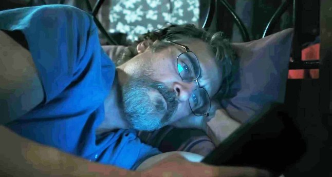 Joaquin Phoenix as Sheriff Joe Cross scrolls on his phone while in bed in a scene from Eddington