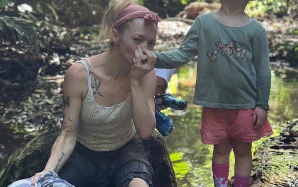 Hannah Spearritt sitting by a river holding her daughter's hand.